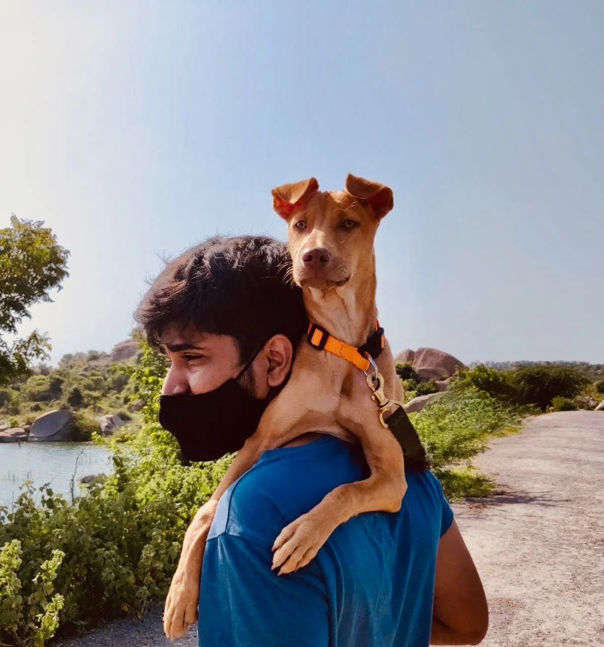 Abhi on a lakeside trail with a tan puppy perched on his shoulders